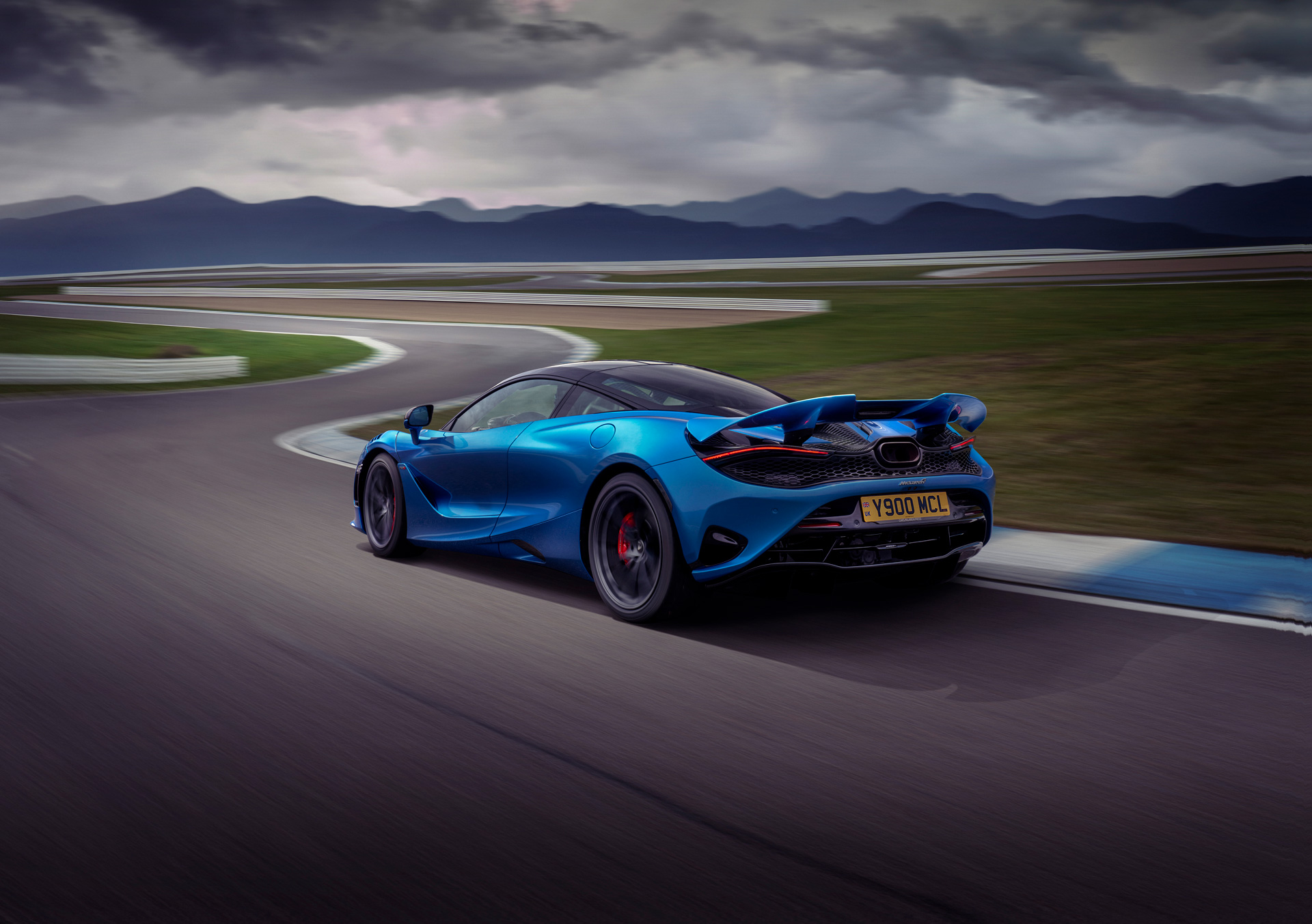 Rear view of blue McLaren 750S driving around a race track at speed, on a cloudy day.
