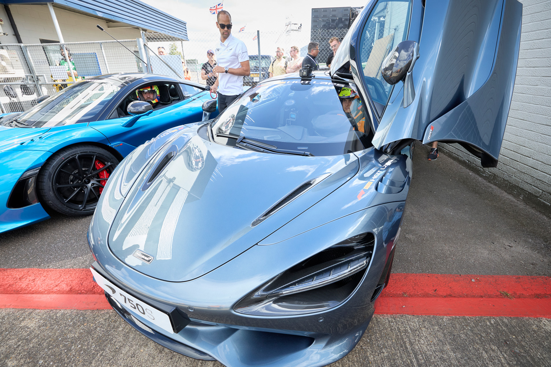 Silver McLaren 750S supercar with open dihedral doors, parked next to a blue McLaren.
