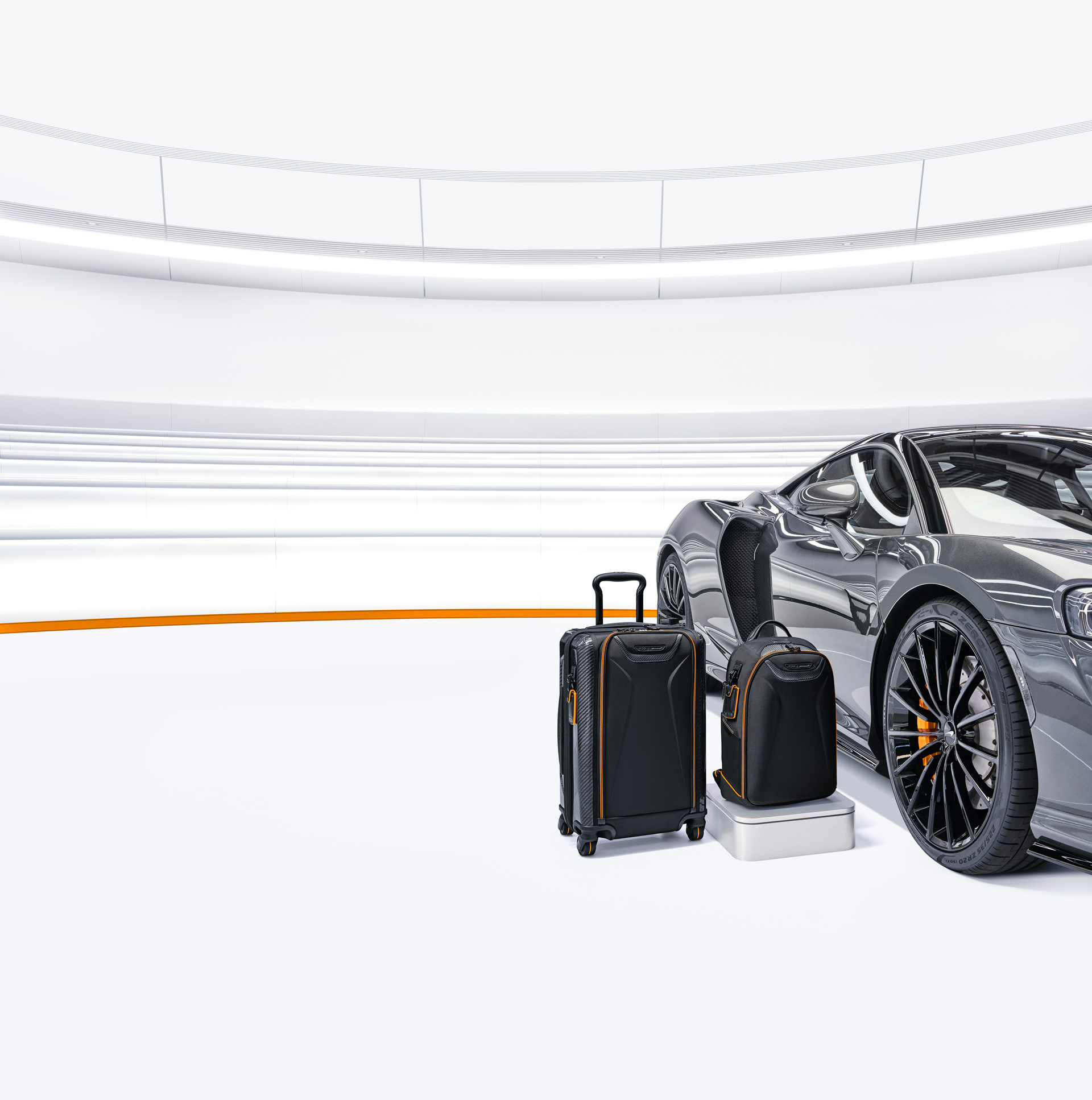 A TUMI | McLaren suitcase and backpack sat next to a grey McLaren in a white environment. 