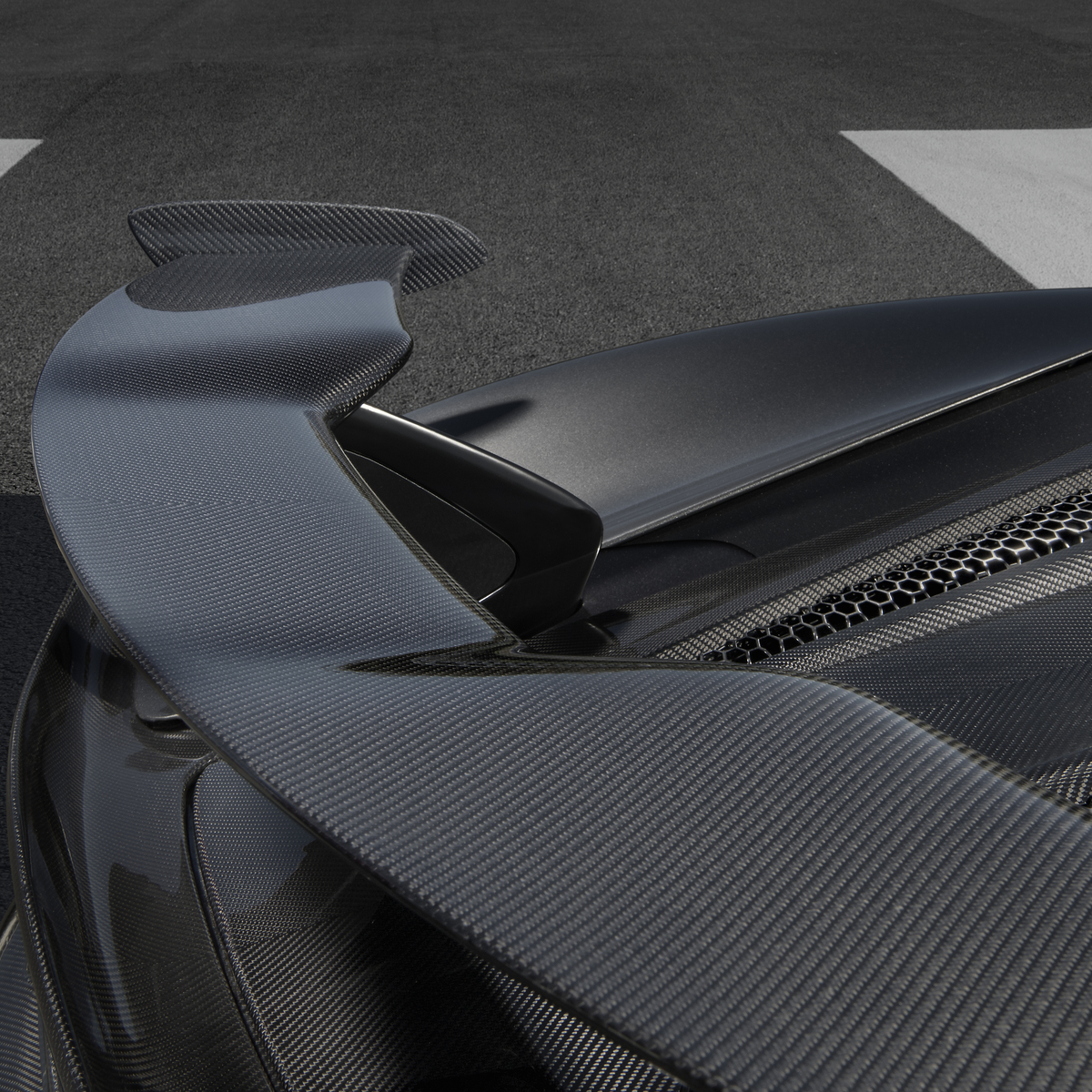 A close-up detail shot of the large carbon fiber rear wing on a dark grey McLaren 600LT, highlighting its intricate weave pattern and aerodynamic design.