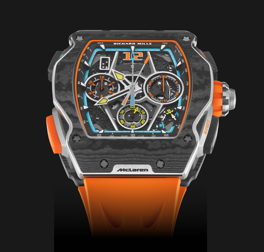 A close-up studio shot of a black and orange Richard Mille McLaren watch, showcasing its intricate dial and textured carbon fiber case.