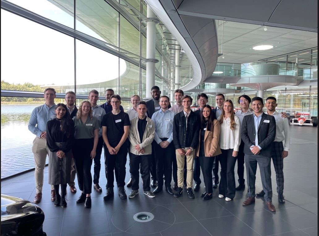 A large group of adults, dressed in a mix of casual and business attire, are posing for a group photo in a modern, well-lit building.