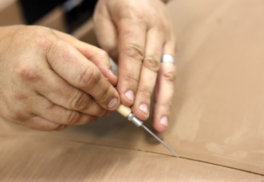 Close-up of a person's hands meticulously working with a tool on a piece of material.