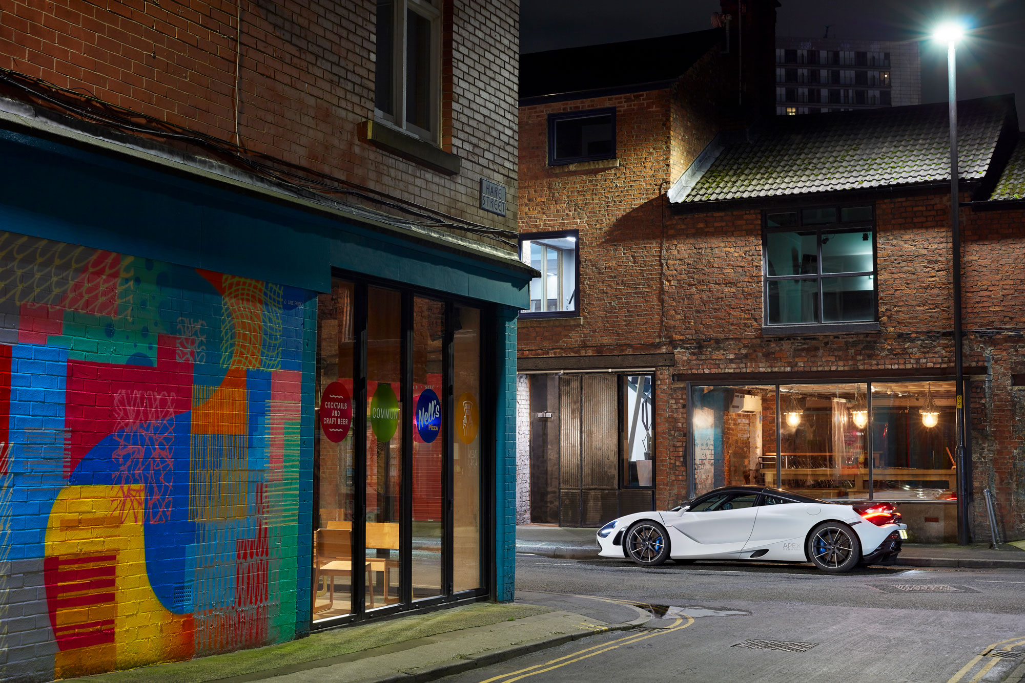 A white McLaren supercar parked on a narrow street at night, with brick buildings in the background.