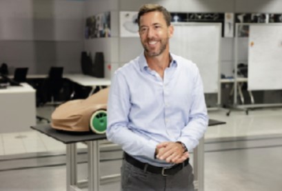  A smiling McLaren employee in a light blue shirt, standing in a workshop next to a clay car model.