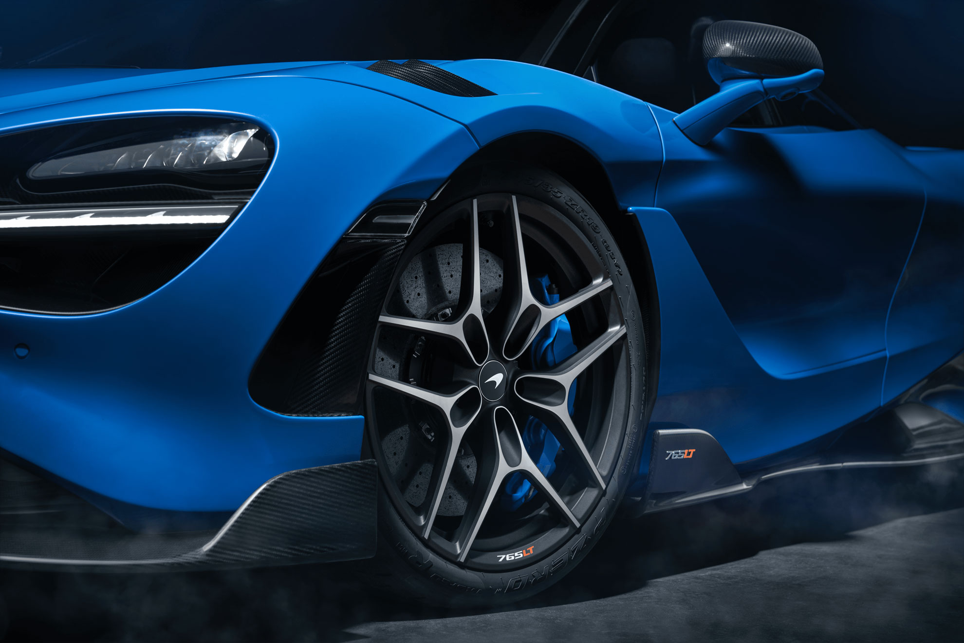 Close-up of the front wheel and blue carbon fiber details of a McLaren 765LT supercar.