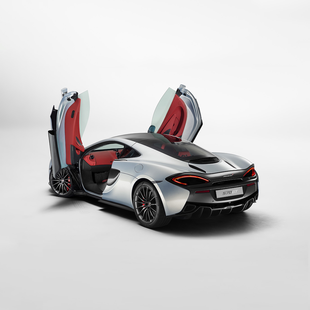 A silver McLaren 570S with its dihedral doors open, showcasing a red and black interior.