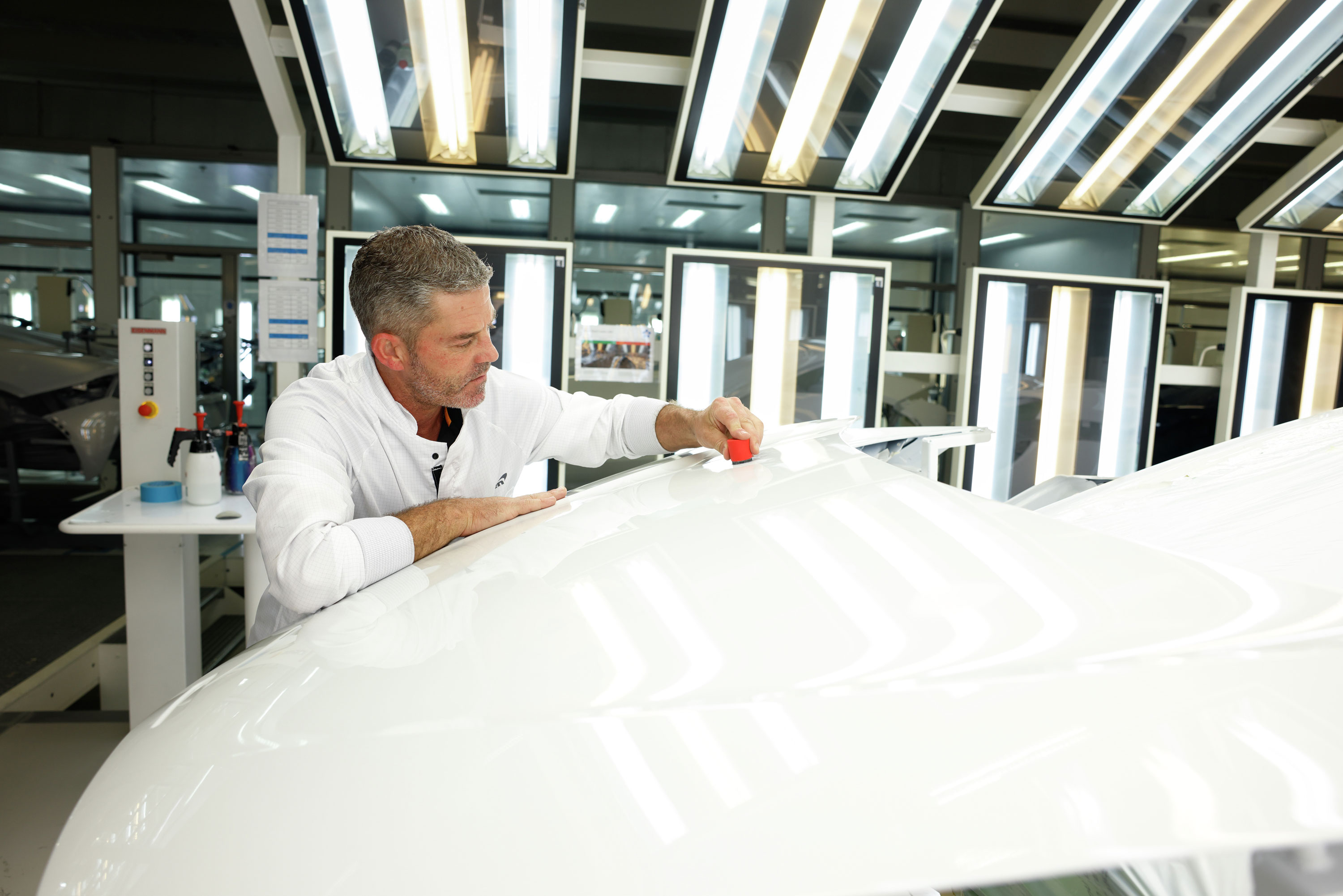 A skilled craftsman carefully polishing the bodywork of a white McLaren supercar in a factory.