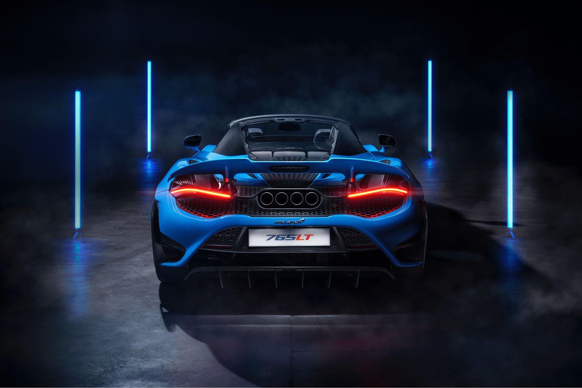 Rear view of a blue McLaren 765LT supercar in a dark studio with blue neon lights.