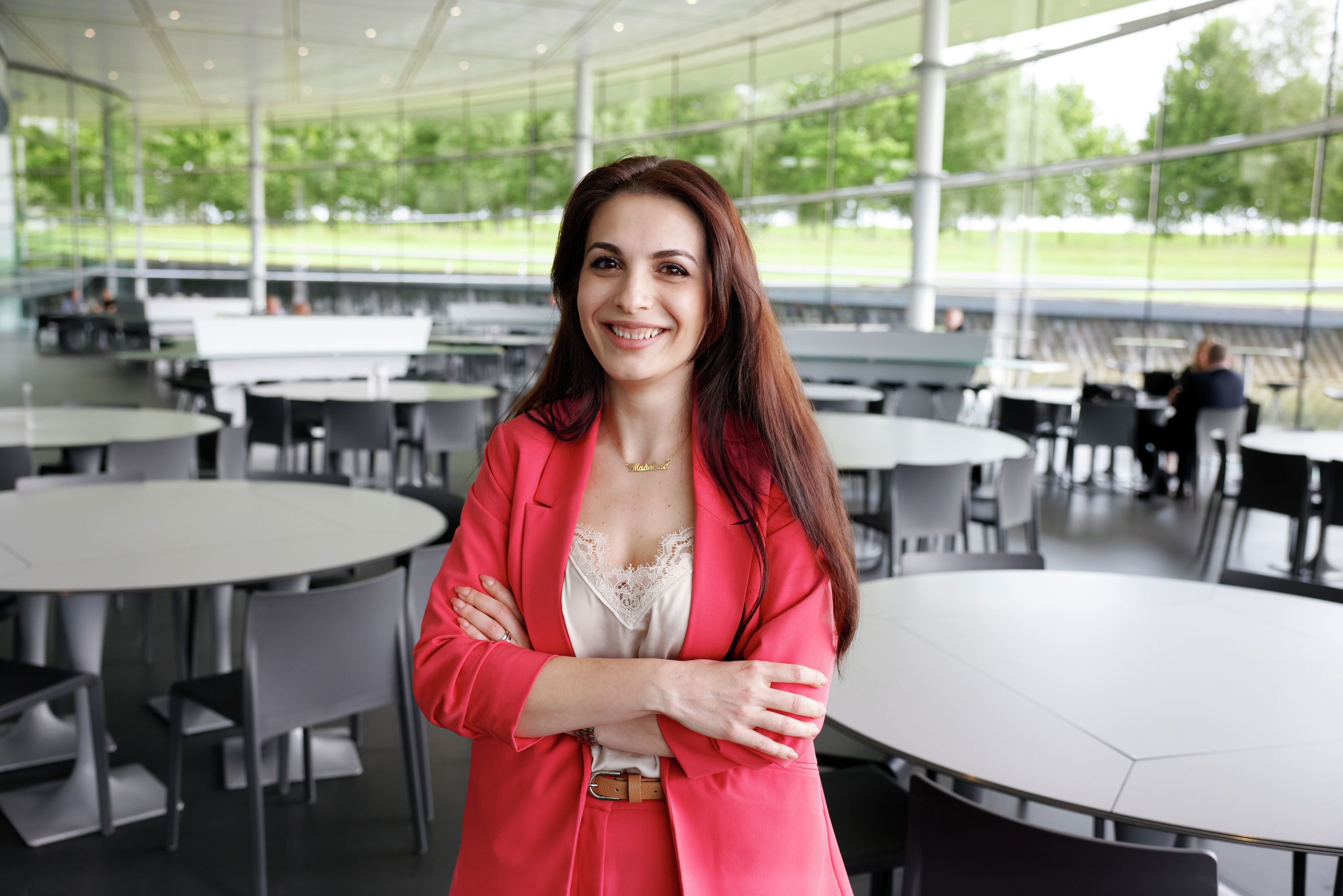 A smiling female McLaren employee in a pink suit, with her arms crossed, standing in the canteen.