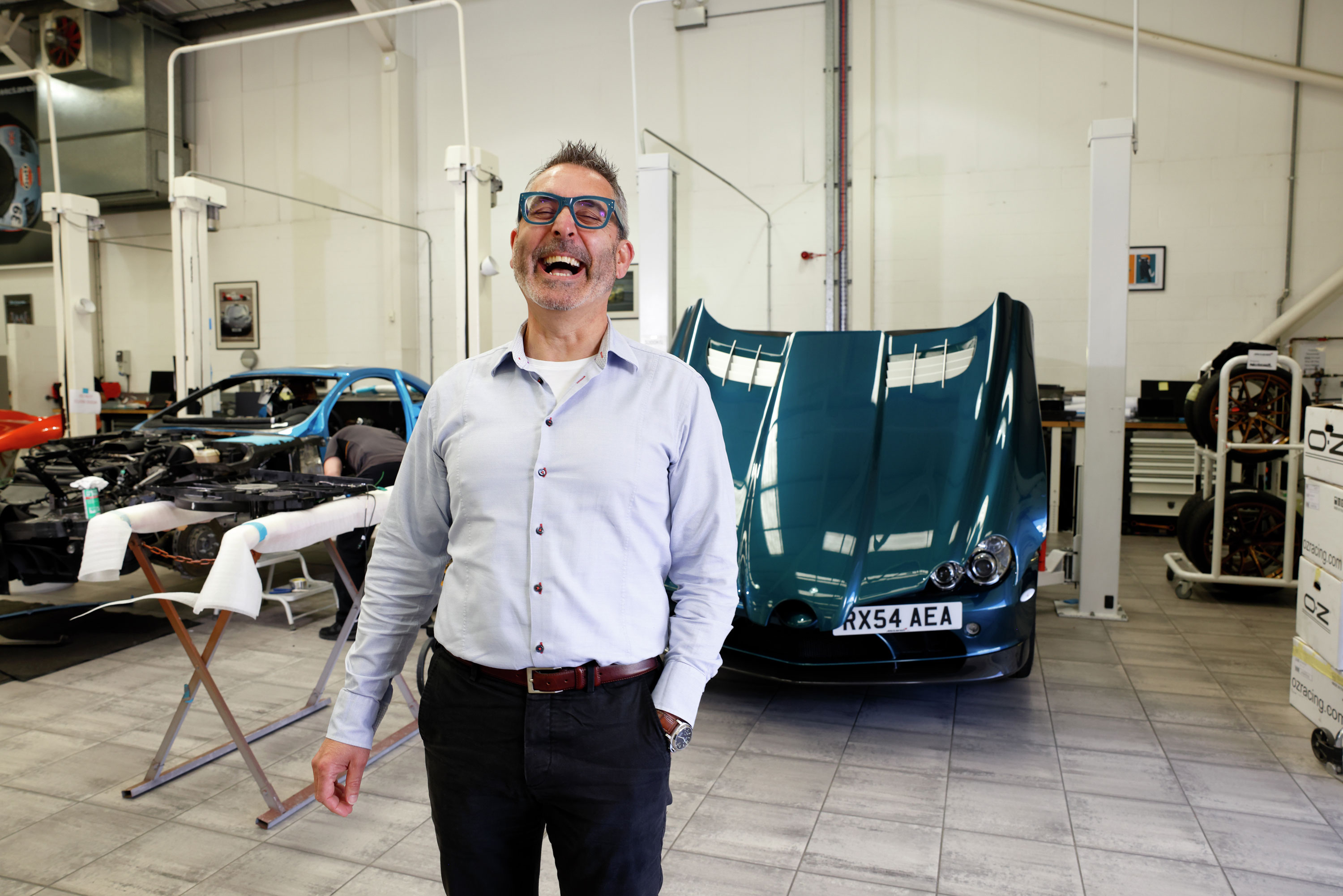 A McLaren employee standing in a workshop with a teal McLaren car in the background.